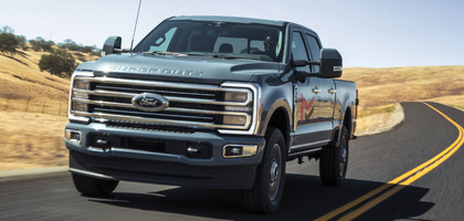 A black 2024 Ford F-350 driving down a road, with dry grass and trees flanking it.