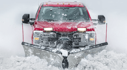 A red 2023 Ford F-250 equipped with the Snow Plow Prep Package and driving through heavy snow.