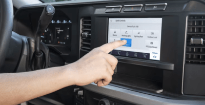 A hand reaching toward the 2023 Ford F-250 Super Duty's infotainment touchscreen to select a custom upfit button.