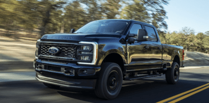 A black 2023 Ford F-250 Super Duty driving down a tree-lined road during the day.