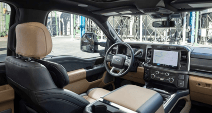 Interior view of the 2023 Ford F-250 Lariat, with two-tone seating and black dashboard showcased. Outside a work-site is visible through the windows.