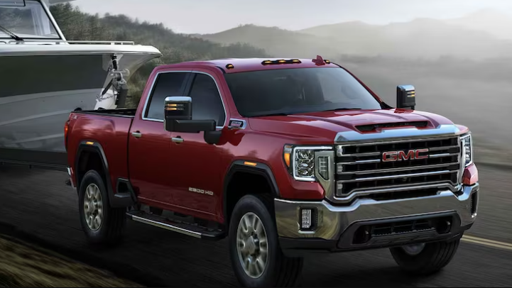 A red 2023 GMC Sierra 2500 pulling a boat along a coastal road.