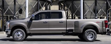 A silver 2023 Ford F-350 Duper Duty parked in front of commercial silos and shown from the side.