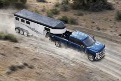 A blue 2023 Ford F-350 Super Duty pilling a trailer down a dirt road, with dust trailing behind it,
