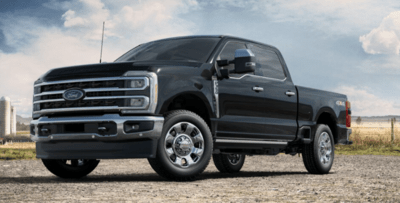 A black 2023 Ford F-350 King Ranch equipped with the Chrome Package and parked on a gravel road, with a field and silos in the background.