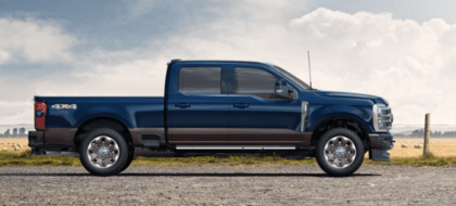 A blue 2023 Ford F-350 King Ranch parked on a gravel road. A field is visible in the background.
