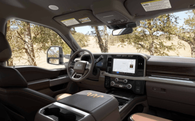 Interior view of the 2023 Ford F-350 King Ranch, with the leather seats, SYNC 4 system, and steering wheel displayed. Beyond the windshield trees are visible.