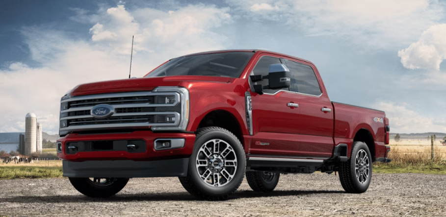 A red 2023 Ford F-350 Limited parked on a gravel road, with a farm and field in the background.