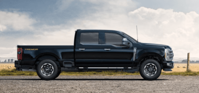 A black 2023 Ford F-350 Platinum equipped with the Tremor Off-Road Package and parked on a gravel road, with a fence and field in the background.