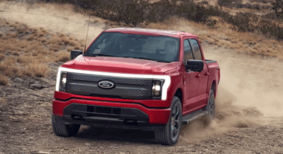 A red 2023 Ford F-150 Lightning driving down a dirt road, with dust trailing behind it.