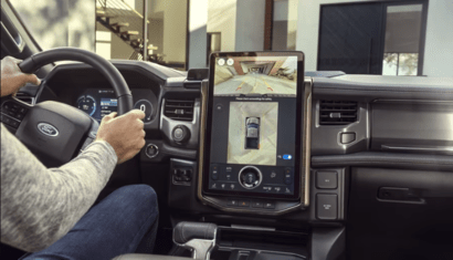 Interior view of the 2023 Ford F-150 Lightning, with the center touchscreen displaying a bird's-eye view of the exterior and hands visible on the steering wheel.