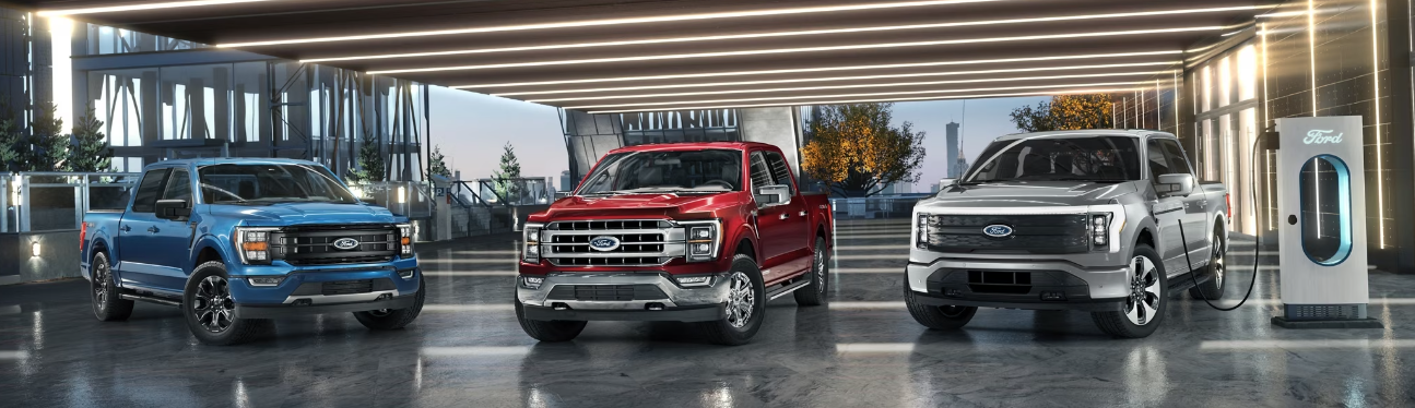 Three 2023 Ford F-150 trucks - one blue, one red, and one silver - parked in a commerical setting.