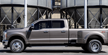 A silver 2024 Ford F-350 Limited shown in profile and parked in front of commercial silos.