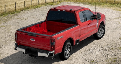 A red 2024 Ford F-350 Lariat Super Duty parked on a gravel road, with a field and a wire fence shown in the background.