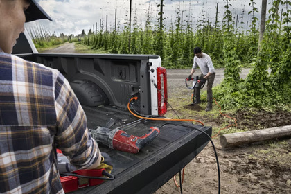 A man using the Pro Power Onboard system on the 2024 Ford F-350 to power tools. Trees and another male worker are seen in the background.