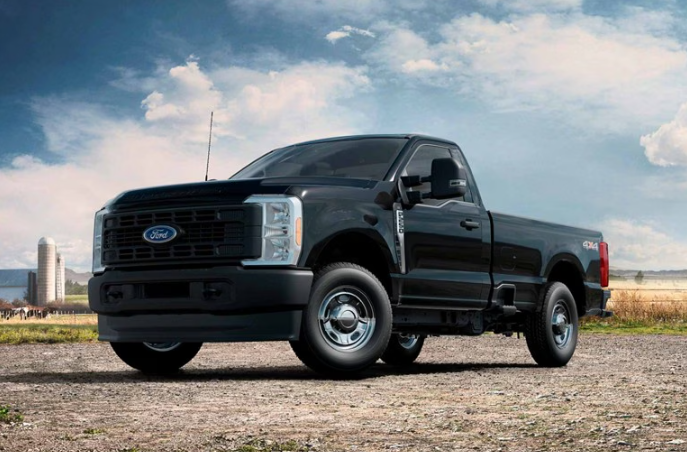 A black 2024 Ford F-350 parked on a gravel road, with a field and farm silos visible in the background.