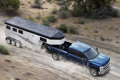 A blue 2024 Ford F-350 shown pulling a white trailer down a dirt road, with dust flying up around it.