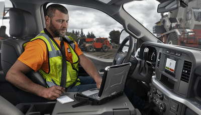 A man wearing a yellow safety vest sitting inside the 2024 Ford F-350 and using a laptop to access the FordPass Connect system.