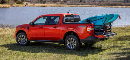 A red 2024 Ford Maverick parked by a lake, with a blue kayak in its bed.