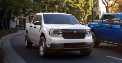 A white 2024 Ford Maverick XL parked beside a blue truck on a tree-lined street.