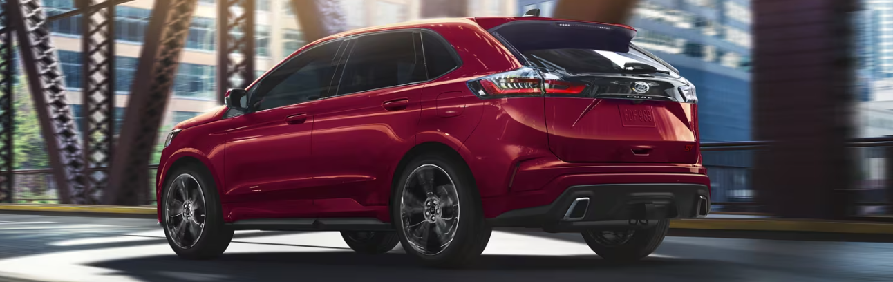 A red 2024 Ford Edge ST driving across a metal bridge and shown from the side.