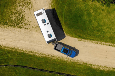 A blue 2024 Ford F-150 pulling a white trailer down a dirt road and shown from an aerial view.