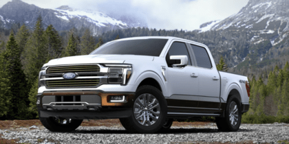 A white 2024 Ford F-150 King Ranch parked on a gravel road, with trees and snow-capped mountains in the distance.