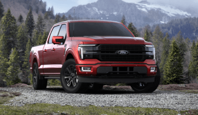 A red 2024 Ford F-150 Platinum parked on a gravel road, with trees and snow-capped mountains visible in the background.