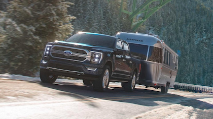 A black 2023 Ford F-150 Limited pulling an Airstream trailer along a mountain road.