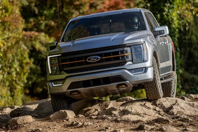 A gray 2023 Ford F-150 Raptor driving over rocks, with trees visible in the background.