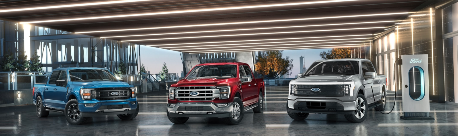 Three 2023 Ford F-150 trucks - one blue, one red, and one silver - parked in an expansive garage.