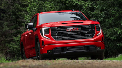 A red 2023 GMC Sierra 1500 driving up a dirt road, with trees in the background.