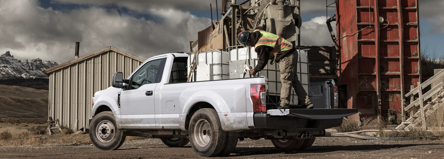 A white 2022 Ford F-350 Super Duty parked at a construction site, with a man securing drums to its bed.