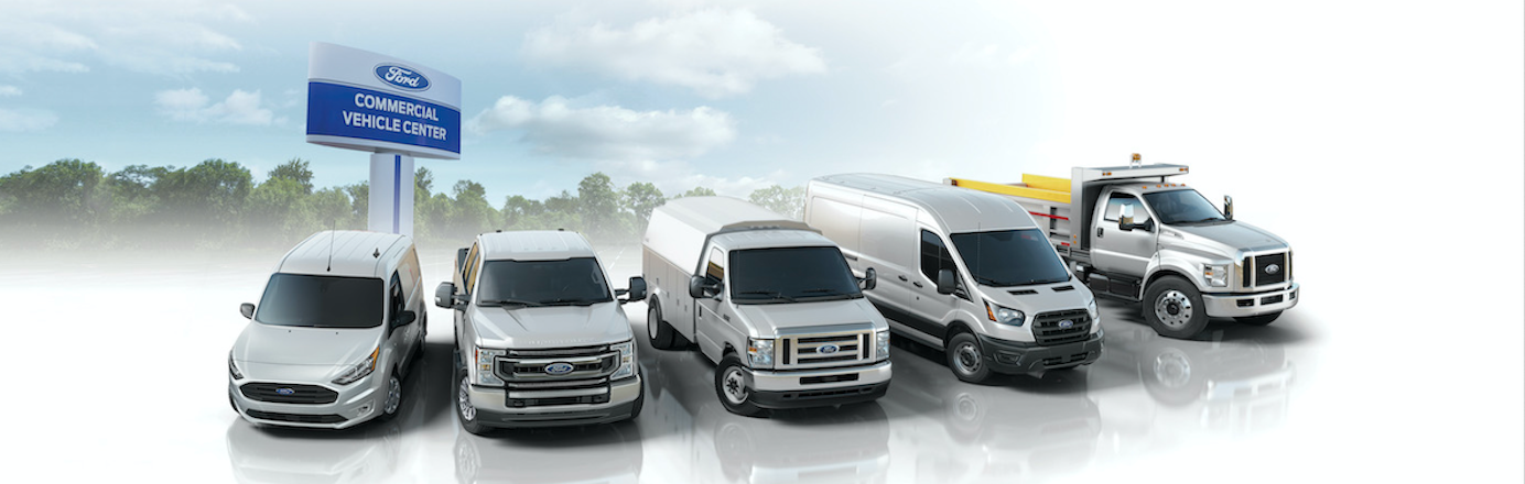 White 2022 Ford heavy-duty vehicles (including the Transit and Super Duty) parked in a semi-circle, with a dealership sign above them that reads: Ford Commercial Vehicles.