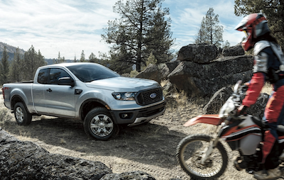 A white 2022 Ford Ranger equipped with the STX Package and parked on a mountain-side. A rider on a dirt bike is pulling up beside it.