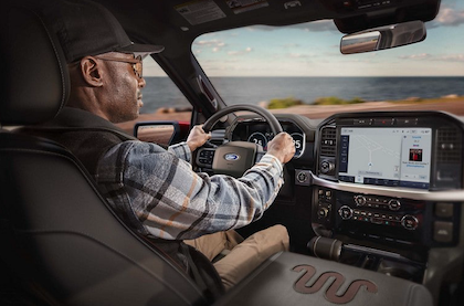 Interior view of the 2023 Ford F-150 Lariat, with a man sitting behind the steering wheel while the SYNC 4 screen displays various media content.