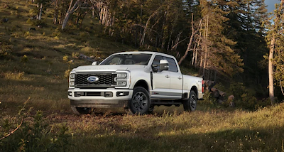 A white 2023 Ford Super Duty parked in a wooded area.